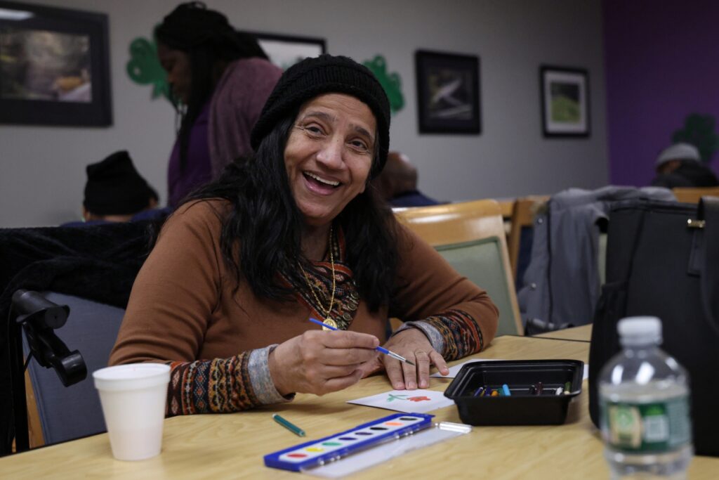 Mumtaz Budwani smiles while a photo is taken of her painting in Rogerson's Adult Day Health program.